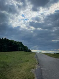 A small road pointing up and with dark trees at the left side and heavy clouds