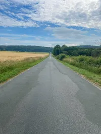 A straigh road climbing up surrounded by fields and forrests