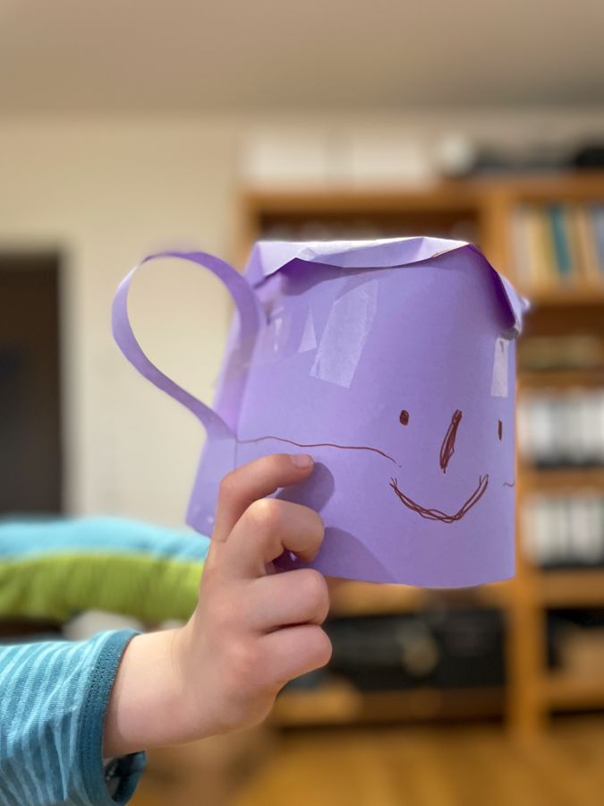 Emil holding a paper-made purple colored teapot with a face drawn on it. The teapot is a teapot-pokemon!