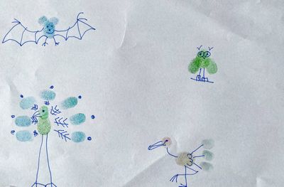 Emil made green, blue, and orange stamps with his colored thumb on a white paper. Then he used a blue fineliner to complete the stamps by drawing animals. A bat and three birds.
