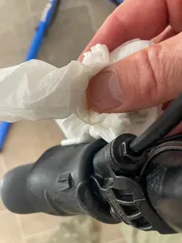 A hand holding a paper towel wiping away oil from the brake shifter