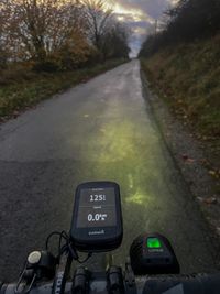 A dropbar handlebar with a mounted computer and battery lights pointing towards a paved rural road in the dark eventing hours.
