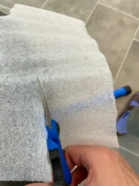 A hand with a scissor cutting a piece from plastic packaging material