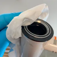 A hand with a paper tower cleaning the top cup from excess grease