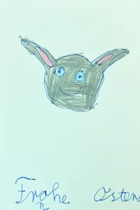 A green holiday card with a drawing of the head of a bunny with long ears and a smiling face. At the bottom of the card is hand written 'Frohe Osrtern', which means happy easter holidays.