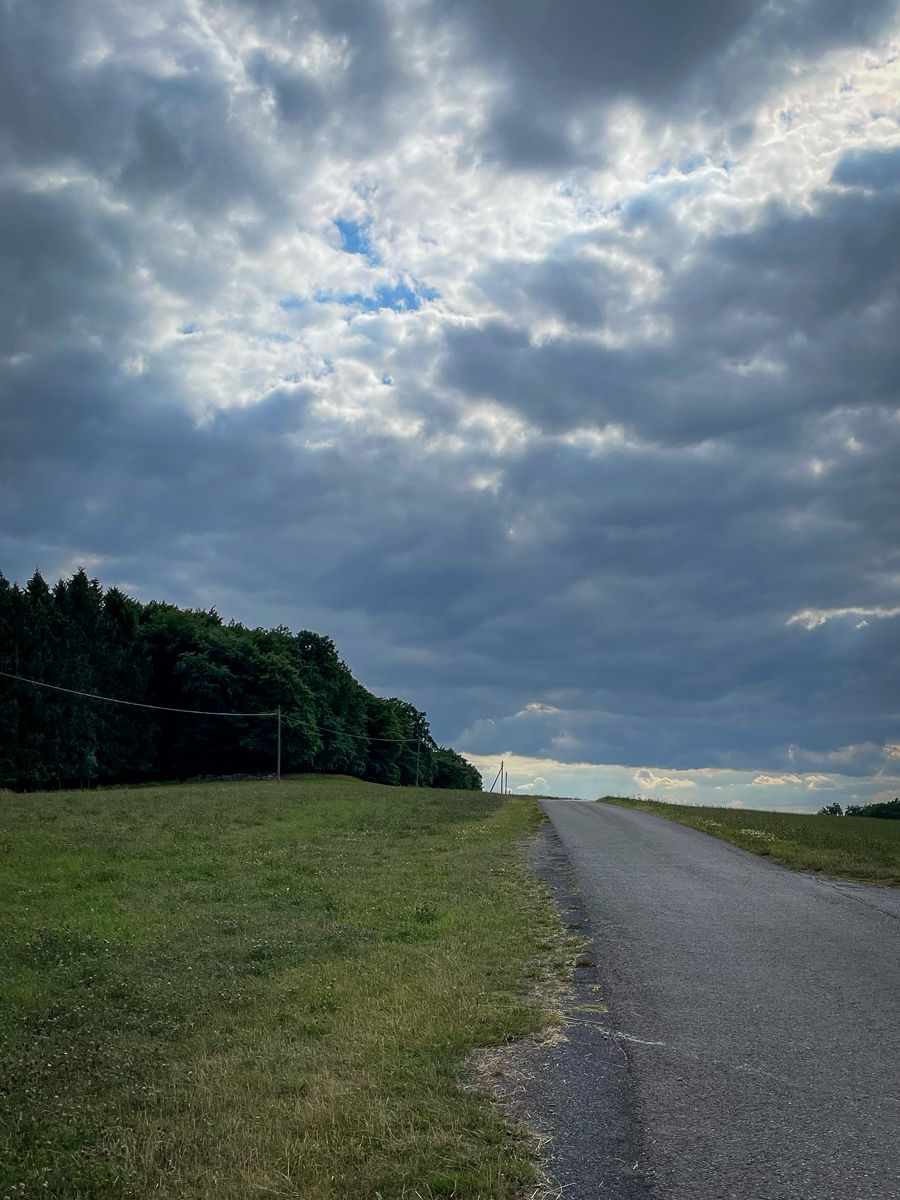 A small road pointing up and with dark trees at the left side and heavy clouds