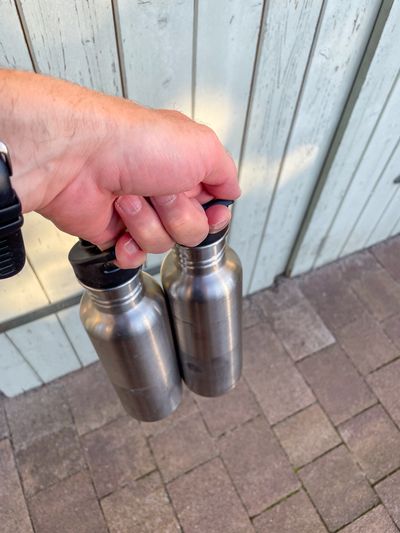 Two Klean Kanteen bottles held with one hand by using the handle on the sport cap of the bottles.