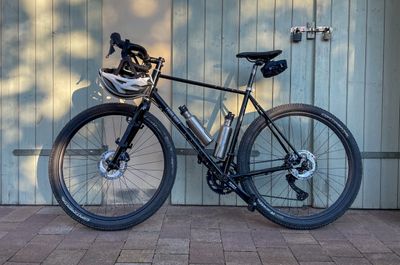 A black Fairlight Secan Gravel bike leaning to a wooden door in the warm evening sun.