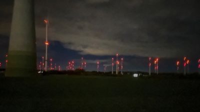 A field of wind turbines in the dark evening with red signaling lights.